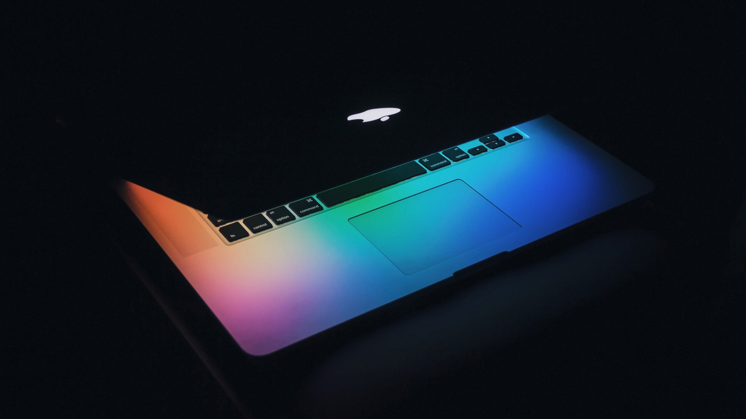 Half closed macbook with rainbow colored light from the screen shining on the keyboard.