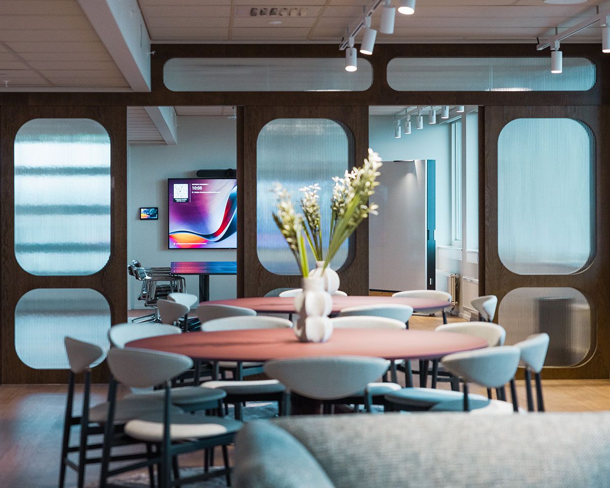 Moderne kontor med sitteplasser og en stor TV bakerst i rommet. 