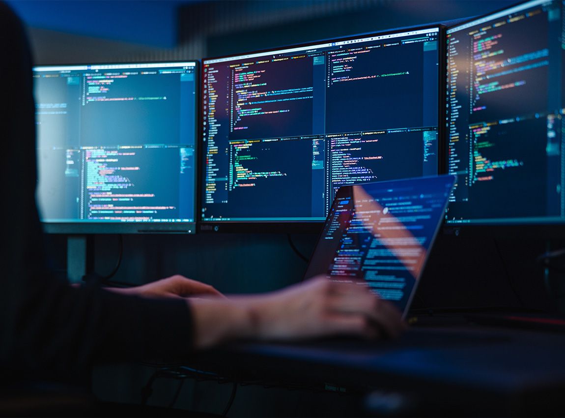 Skrivebord med skjermer som viser kode med hendene til en person som skriver på tastaturet.