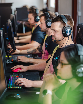 Spelare med hörlurar tävlar vid datorer, fokuserar på skärmar och tangentbord med färgglada ljus.