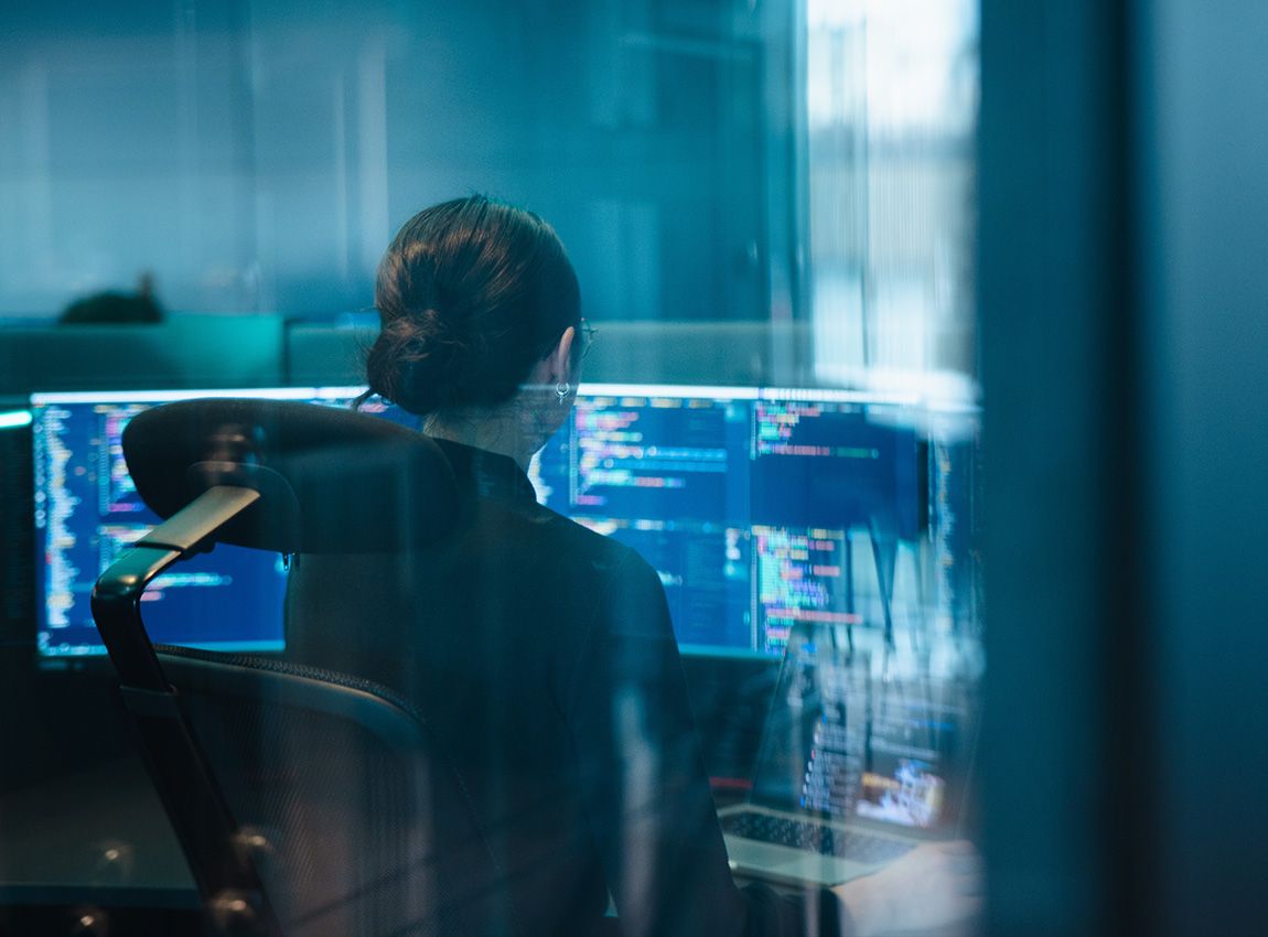 En dame som koder, sett gjennom et vindu. 