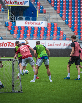Fotbollsspelare i färgade västar spelar fotboll på en stadion.